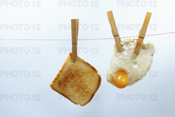 Toasted bread and fried egg are hanging from a clothesline with wooden clothespins, representing a unique breakfast scenario