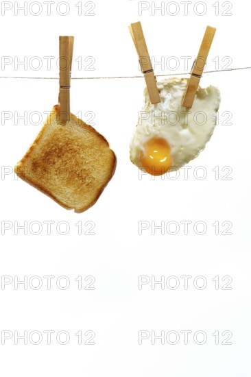 Toasted slice of bread and fried egg hanging from a clothesline on a white background, representing a simple and quick breakfast solution