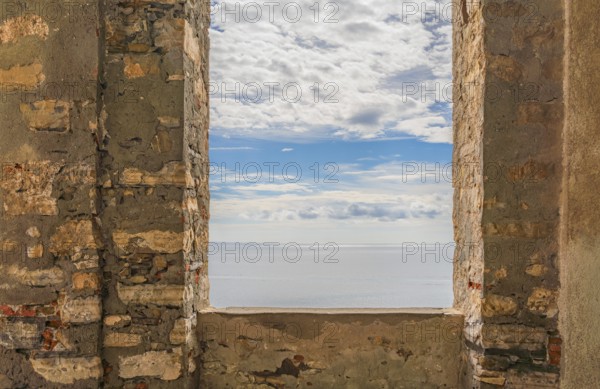 Sunny mediterranean sea scenery seen through a window opening in a historic wall seen in Liguria, Italy