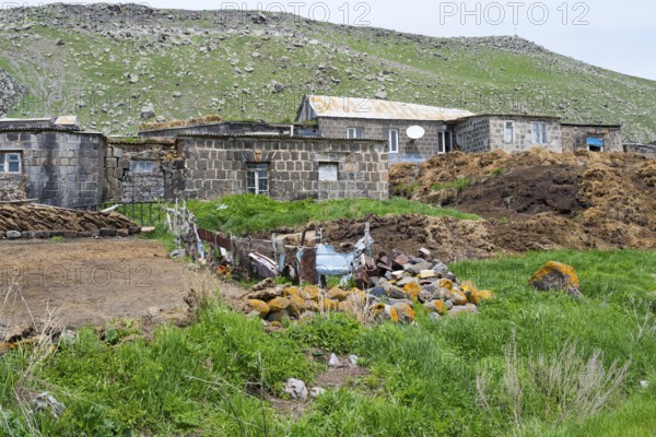 Stone house in a rural area surrounded by green hills and rocks, cow dung in front, Ardenis, Shirak province, Armenia