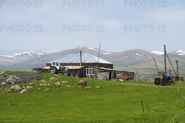A farm with tractors and a stone house in front of a mountain landscape, Zorakert, Lake Arpi, Shirak Province, Armenia