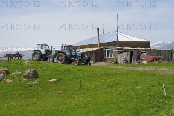 Two tractors standing on a green field next to a farmhouse and a barn, Zorakert, Lake Arpi, Shirak Province, Armenia
