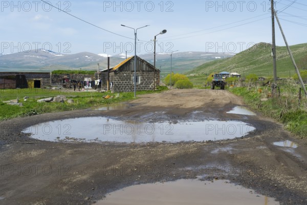 A muddy road with large puddles leads through a village with mountains in the background, Zorakert, Lake Arpi, Shirak Province, Armenia