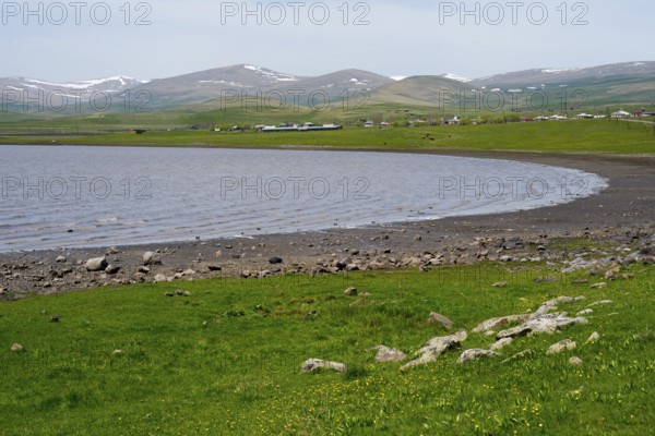 Tranquil lake with a view of green hills and distant mountains on the horizon, Lake Arpi, Shirak Province, Armenia