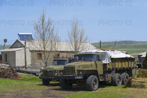 Large lorries parked on a farm in front of a stone building surrounded by green countryside, Gaz 53 or 52 on the left, Ural 4320 on the right, Berdashen, Lake Arpi, Shirak Province, Armenia