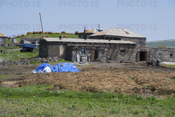 Rural farm with stone buildings and thatch, surrounded by green landscape, house, cow dung in front, in Berdashen, Lake Arpi, Shirak Province, Armenia