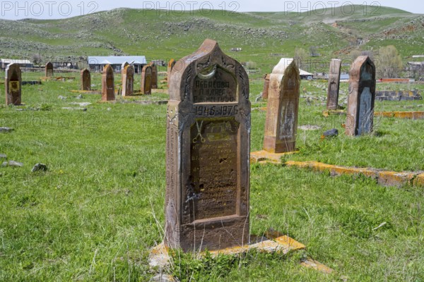 A well-preserved old gravestone on green grass in front of a hilly landscape with several gravestones, old cemetery, Aghvorik, Shirak province, Armenia