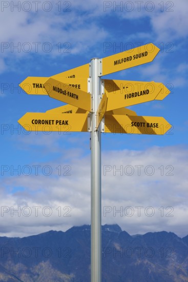 Yellow signposts with various destinations against a backdrop of blue sky and mountains, Queenstown, Queenstown-Lakes District, Otago, South Island, New Zealand