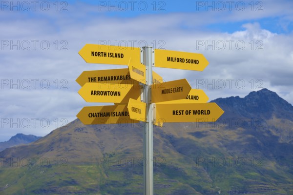 Yellow signpost in a mountain landscape, showing directions to different places, Queenstown, Queenstown-Lakes District, Otago, South Island, New Zealand