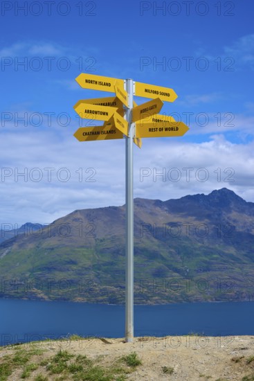 A signpost on a hill shows yellow signs in different directions, Queenstown, Queenstown-Lakes District, Otago, South Island, New Zealand