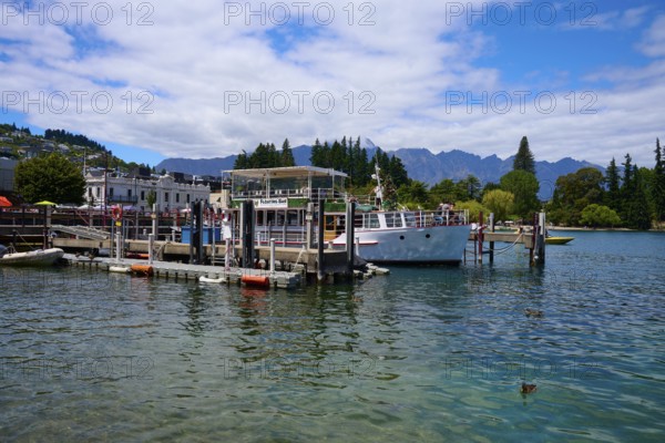 Harbour with boats and buildings on calm lake under partly cloudy sky, Queenstown, Queenstown-Lakes District, Otago, South Island, New Zealand