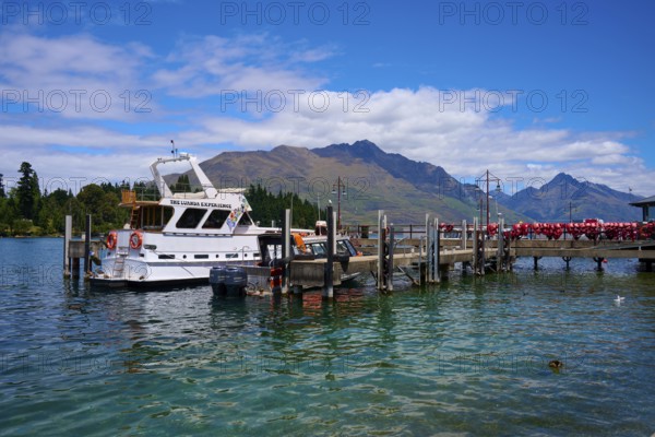 Boat at a jetty on a tranquil lake with surrounding mountain scenery, Queenstown, Queenstown-Lakes District, Otago, South Island, New Zealand