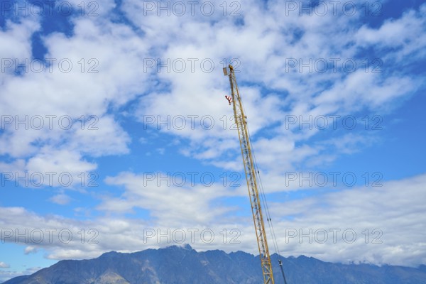 A tall construction crane erected against a cloudy sky with a mountain backdrop, Queenstown, Queenstown-Lakes District, Otago, South Island, New Zealand