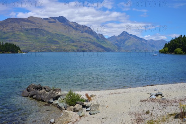 Clear lake with beach and mountains surrounded by natural beauty, Queenstown, Queenstown-Lakes District, Otago, South Island, New Zealand