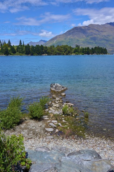 Rocks on the shore of a lake with mountains in the background and a clear atmosphere, Queenstown, Queenstown-Lakes District, Otago, South Island, New Zealand