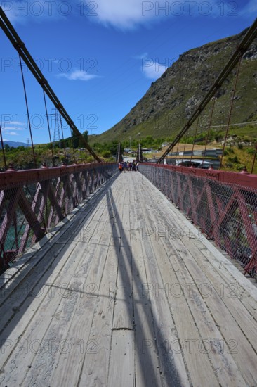 Wooden footbridge with red railing, shadows and mountain background, Kawarau Gorge Suspension Bridge, Kawarau River, Queenstown, Otago, South Island, New Zealand