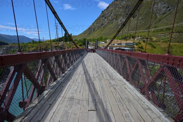 Wooden footbridge with cables and mountain backdrop on a clear, sunny day, Kawarau Gorge Suspension Bridge, Kawarau River, Queenstown, Otago, South Island, New Zealand