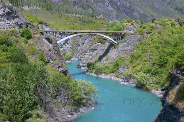A bridge spans a turquoise-coloured river in a green and rocky landscape, Kawarau River, Queenstown, Otago, South Island, New Zealand