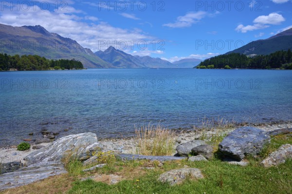 Tranquil seascape with grassy rocks and mountains in the background, Queenstown, Queenstown-Lakes District, Otago, South Island, New Zealand