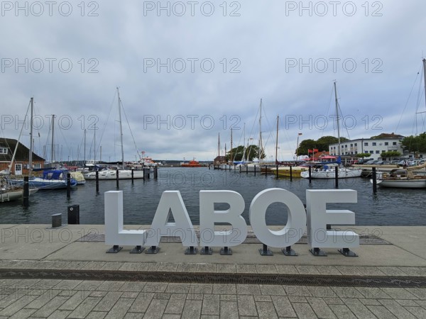 LABOE lettering at the edge of the harbour, surrounded by sailing boats and a cloudy sky, Laboe, Kiel Fjord, Schleswig-Holstein, Germany