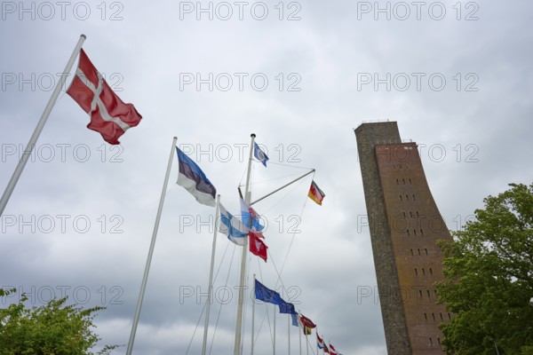 National flags next to a high brick tower under a cloudy sky, Naval Memorial, Laboe, Kiel Fjord, Schleswig-Holstein, Germany
