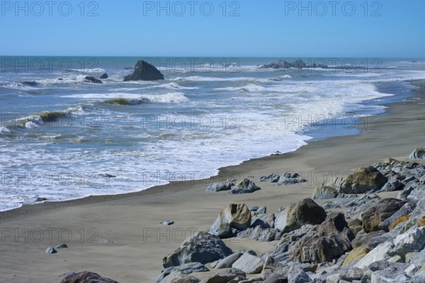 The waves gently lap against a wide sandy beach with scattered rocks, West Coast, South Island, New Zealand