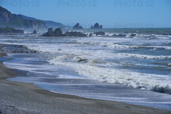 Beach with powerful waves and rocks under a clear blue sky, West Coast, South Island, New Zealand