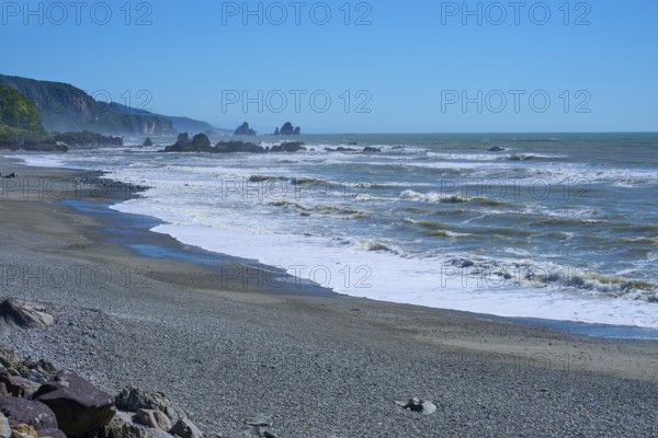 Extensive stretch of coastline with rough waves and rocks under a clear sky, West Coast, South Island, New Zealand