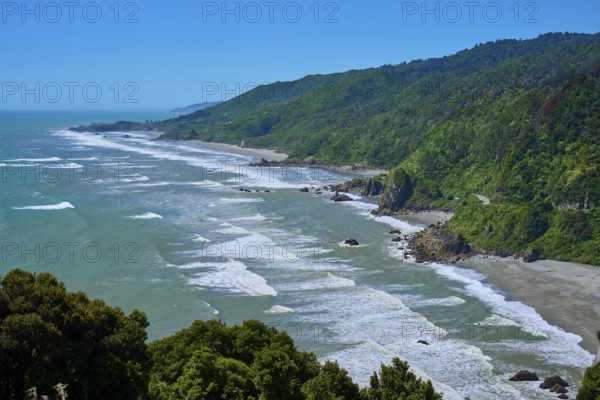 Long coastline with green hills and gentle waves under a clear blue sky, West Coast, South Island, New Zealand
