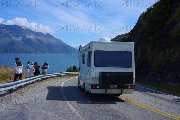 People enjoying travelling and a motorhome driving on a road along a lake surrounded by mountains, Devil's Staircase Lookout Point, Kingston, Lake Wakatipu, Queenstown-Lakes District, Otago, South Island, New Zealand
