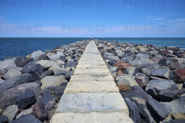 A stony path leads into the sea, surrounded by a sunny coastal landscape, Mana Bay, Patea, Taranaki, North Island, New Zealand