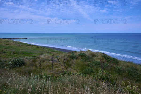White sandy beach with grassy coastline and gentle waves under a cloudy sky, Mana Bay, Riverview Lookout, Patea, Taranaki, North Island, New Zealand