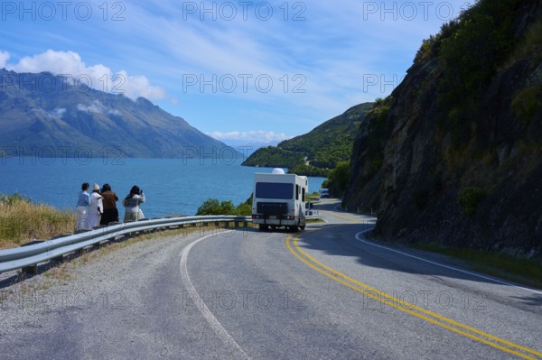 People enjoying travelling and a motorhome on a winding road next to a lake surrounded by mountains, Devil's Staircase Lookout Point, Kingston, Lake Wakatipu, Queenstown-Lakes District, Otago, South Island, New Zealand