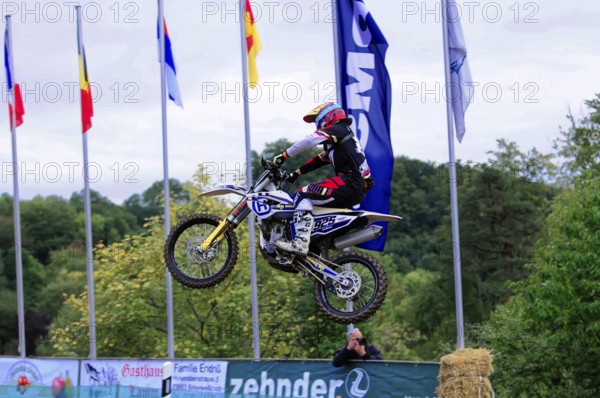Motocross, Rudersberg, Baden-Württemberg, Germany, Europe, Motocross rider jumps with motorbike in front of flags. Green landscape in the background, Rudersberg motocross
