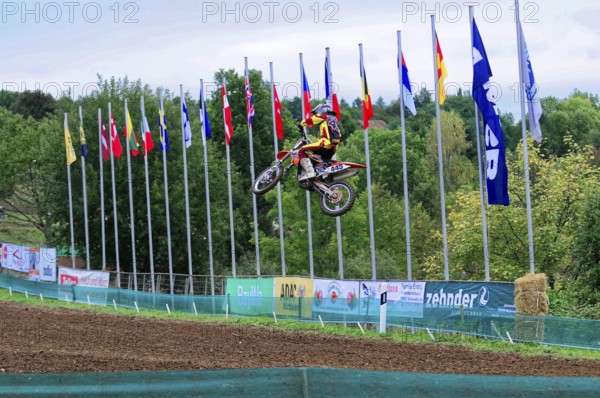 Motocross, Rudersberg, Baden-Württemberg, Germany, Europe, A motorcyclist jumps into the air while numerous flags fly in the background, Rudersberg Motocross