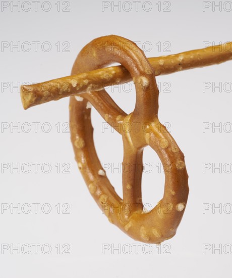 Small lye pretzel hanging on a salt stick in light back