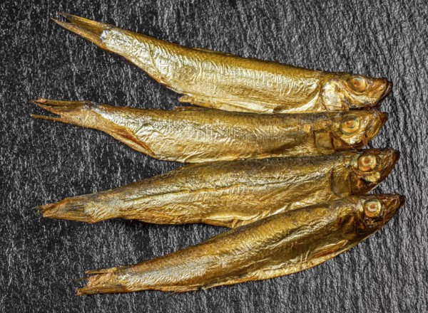 Arrangement with fresh smoked sprats on dark stone slab