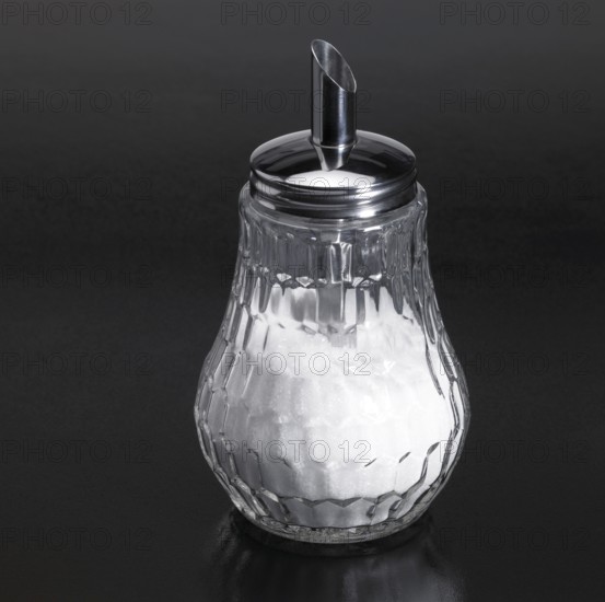 Studio photography of a sugar sprinkler made of glass and metal in dark reflective back
