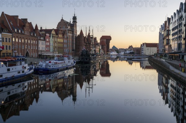 Waterfront promenade with reflection at sunrise in the Old Town, Brama Zuraw crane gate, Motlawa River, Gdansk, Gdansk, Poland