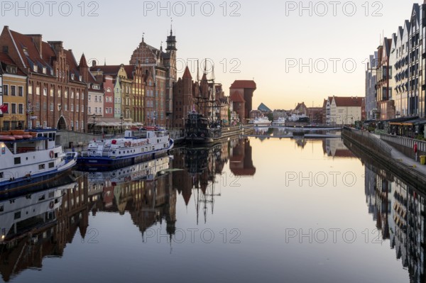 Waterfront promenade with reflection at sunrise in the Old Town, Brama Zuraw crane gate, Motlawa River, Gdansk, Gdansk, Poland
