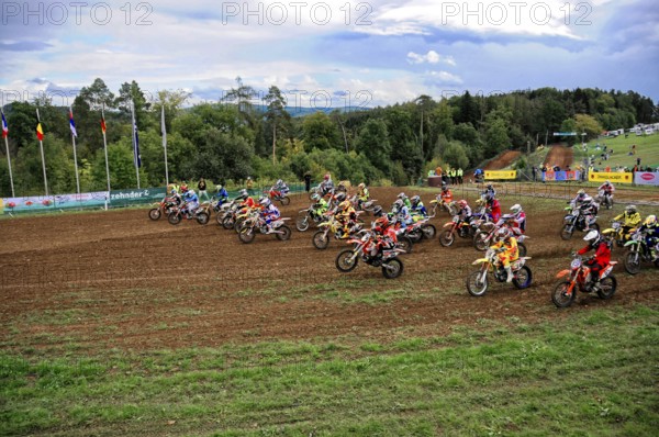 Motocross, Rudersberg, Baden-Württemberg, Germany, Europe, Motocross riders accelerate after the start of a race, surrounded by green landscape and flags, Rudersberg motocross