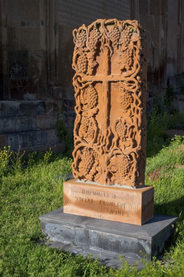 A detailed engraved red gravestone with a cross motif stands on a grassy area in the sunlight, cross stone, Khachkar, Marmashen Monastery, Marmashen Vank, Shirak Province, Armenia