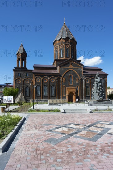 A red church with classical architecture and a stone monument under a clear sky, Church of the Holy Saviour, Church of the Saviour and monument to the victims of the earthquake in Spitak, Gyumri, Gyumri, Shirak province, Armenia
