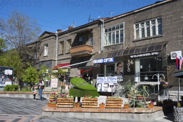Pedestrian zone with optical shop and advertising signs, flanked by concrete buildings and trees, Gyumri, Gyumri, Shirak Province, Armenia