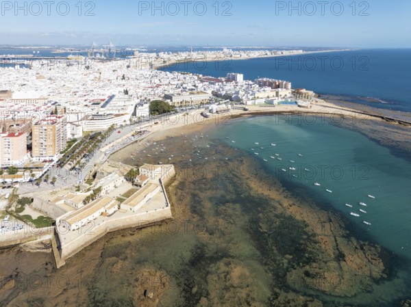 The town of Cádiz with the old quarter in the foreground. Prominent the Santa Catalina castle, the Caleta beach, the old Balneario de la Palma and the fishing boats at low tide. Aerial view. Drone shot. Cádiz province, Andalusia, Spain