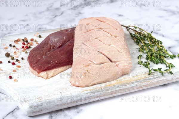 Fresh raw duck breasts, spread on a wooden cutting board, with herbs and spices, on a white marble surface