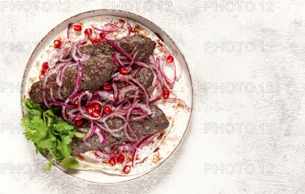 Grilled kebabs topped with onions and pomegranate on a white plate in a bright kitchen setting