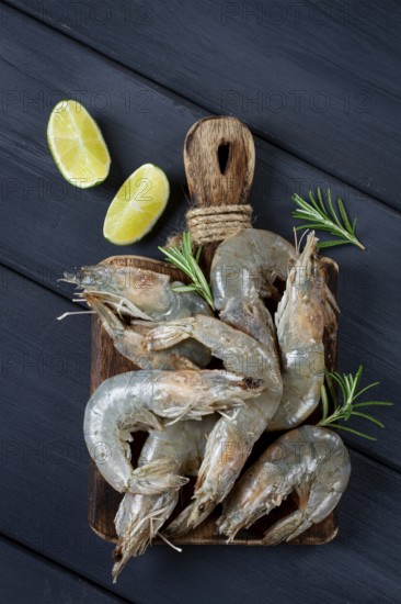 Fresh raw, white-footed shrimp, tiger prawns vannamei, on a wooden cutting board, with lime slices, and seasonings