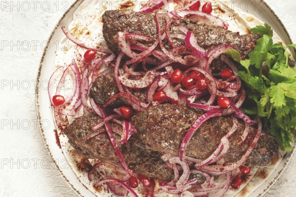 Grilled kebabs topped with onions and pomegranate on a white plate in a bright kitchen setting