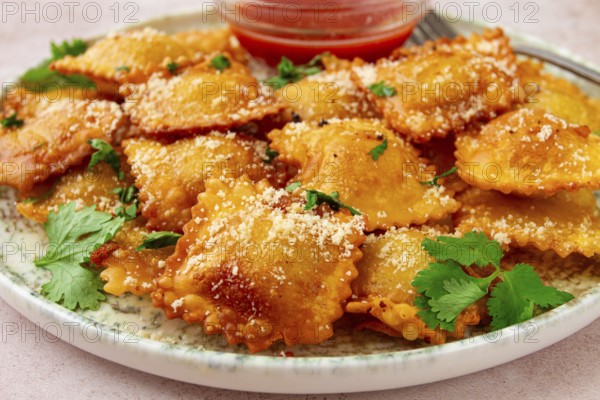 Fried ravioli with parmesan cheese, served with red sauce and garnished with herbs, on a light background, no people